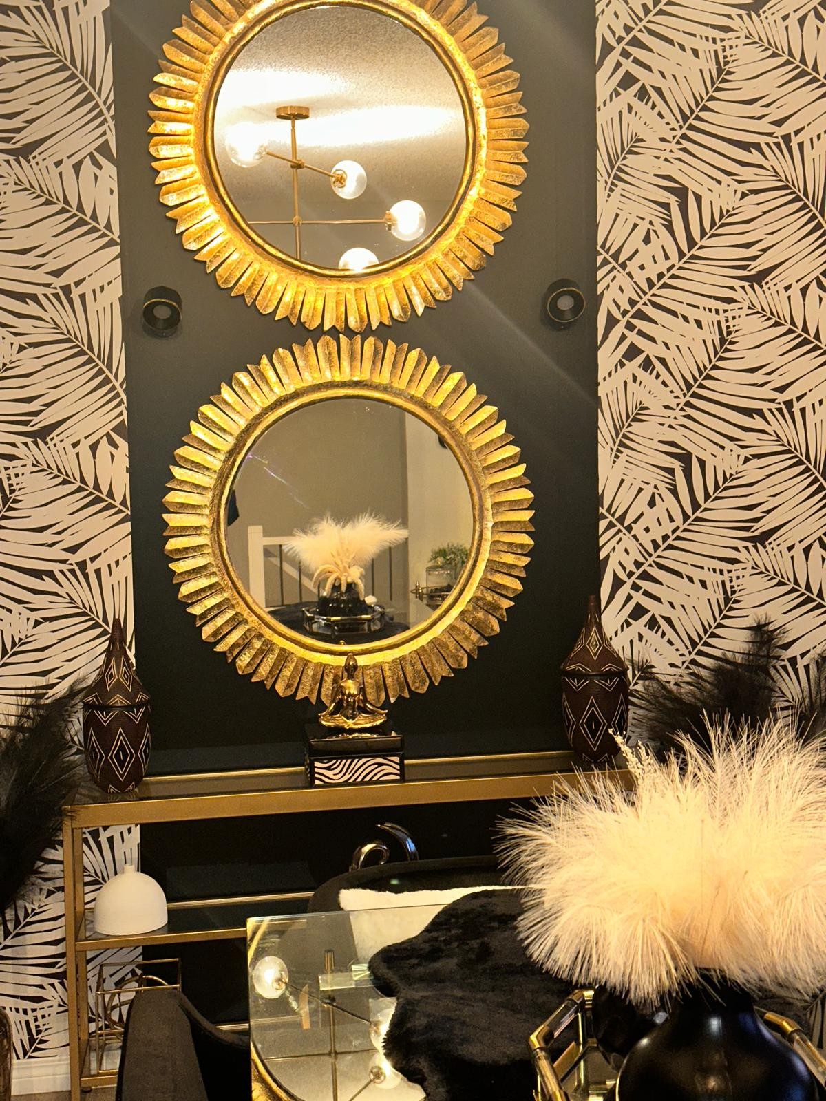 Twin gold sunburst mirrors above black console with carved vessels