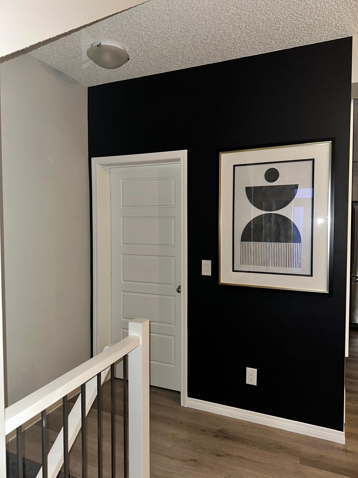 Black accent wall with graphic framed abstract art at top of stair